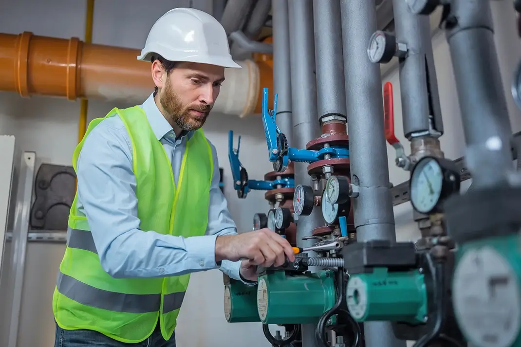 Expert plumber fixing a hot water pipe in the technical area of heating system.