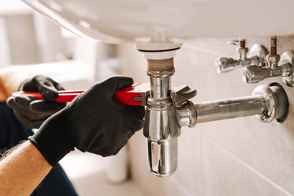 Professional plumber repairing a leaking sink drain pipe with a wrench.